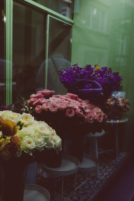 A display of fresh floral arrangements inside a flower shop storefront, with bouquets of various colours including white, pink, and purple roses, along with other blooms. The flowers are arranged in d